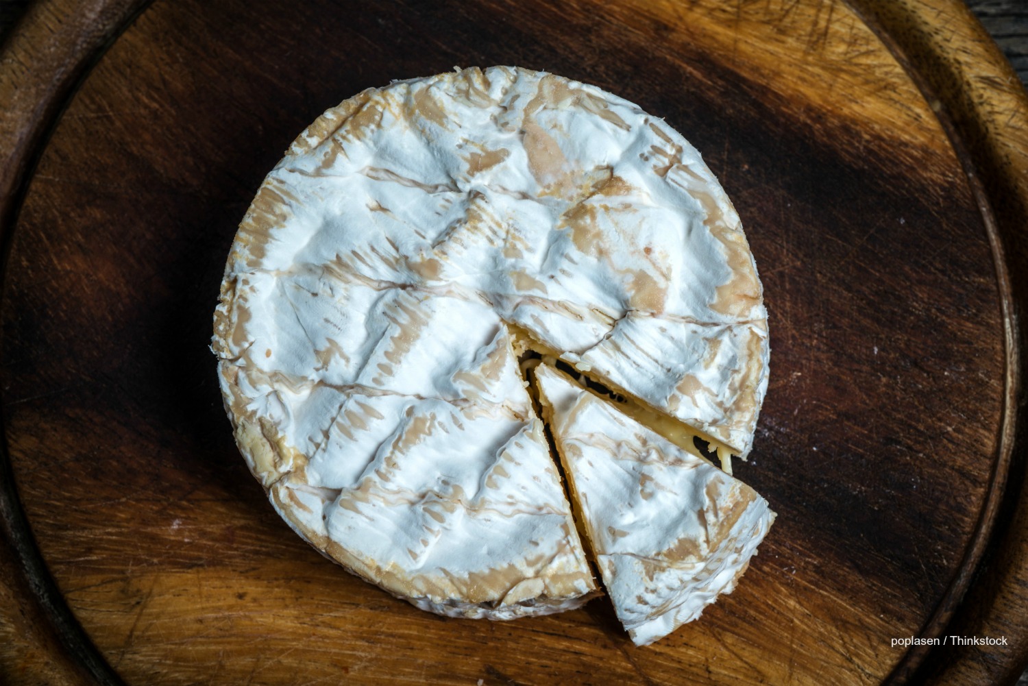 Round of brie cheese on rustic wooden cutting board , top view